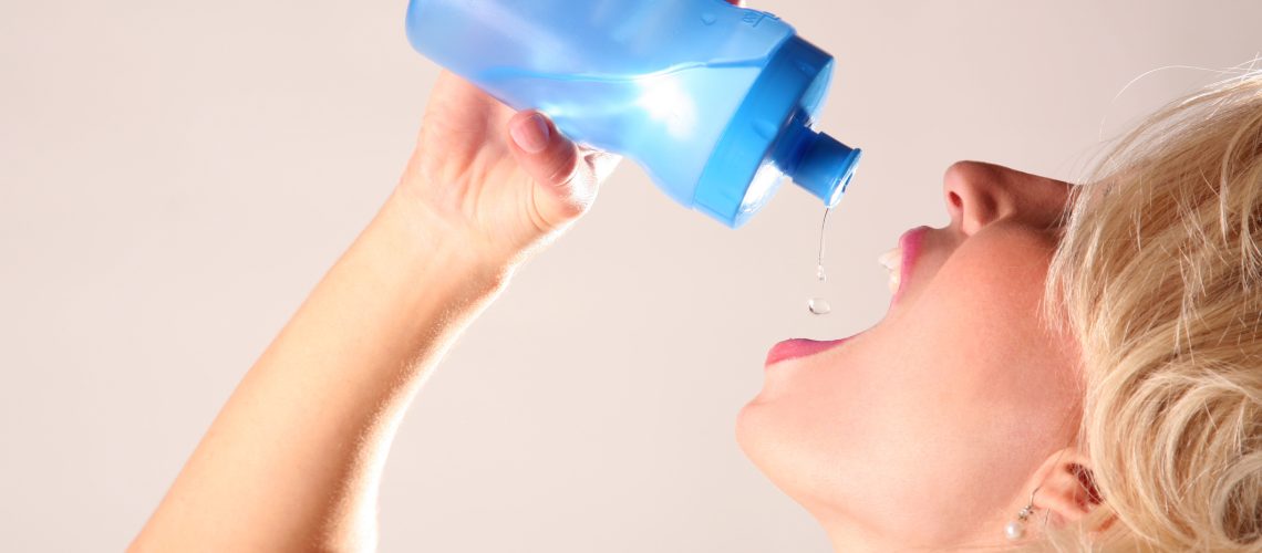 An attractive thirty-something female drinks water from plastic water bottle after a fitness work-out.