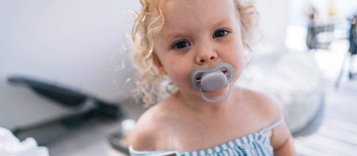 Portrait of baby girl sucking on soother outdoors on beach vacation